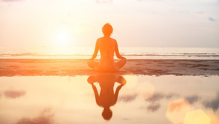 person meditating on the beach with a sunrise
